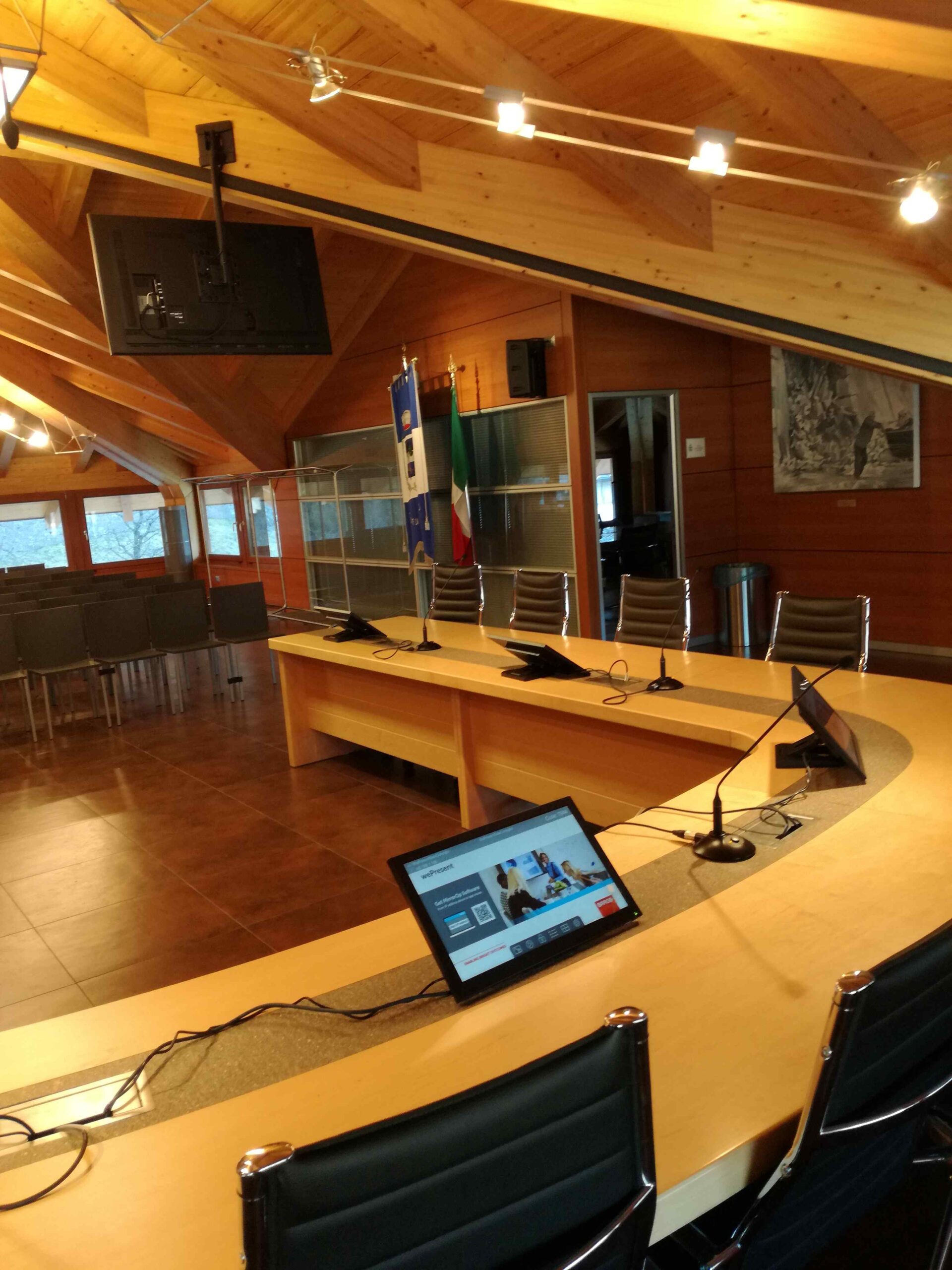 Panoramica della sala consigliare di Albiano con bandiere, monitor e postazioni conferenza