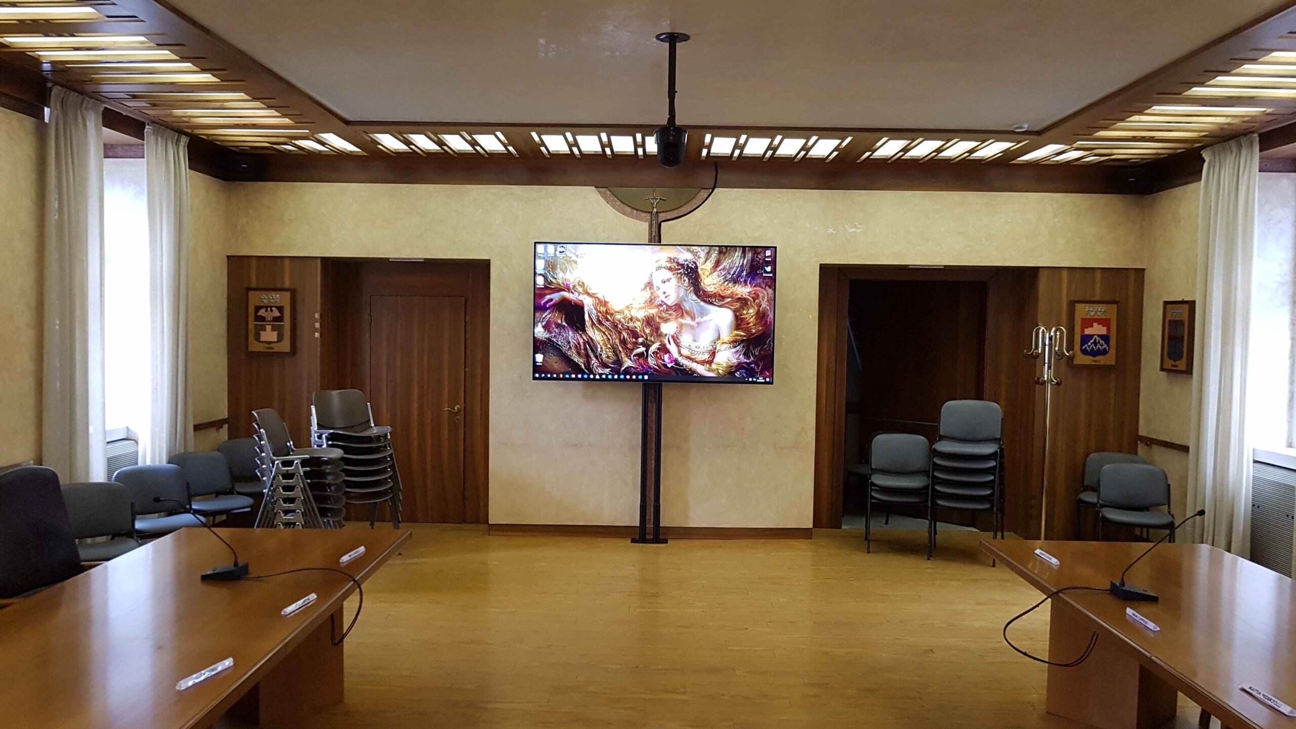 Sala consigliare di Tione con grande monitor a soffitto e tavoli con microfoni conferenza