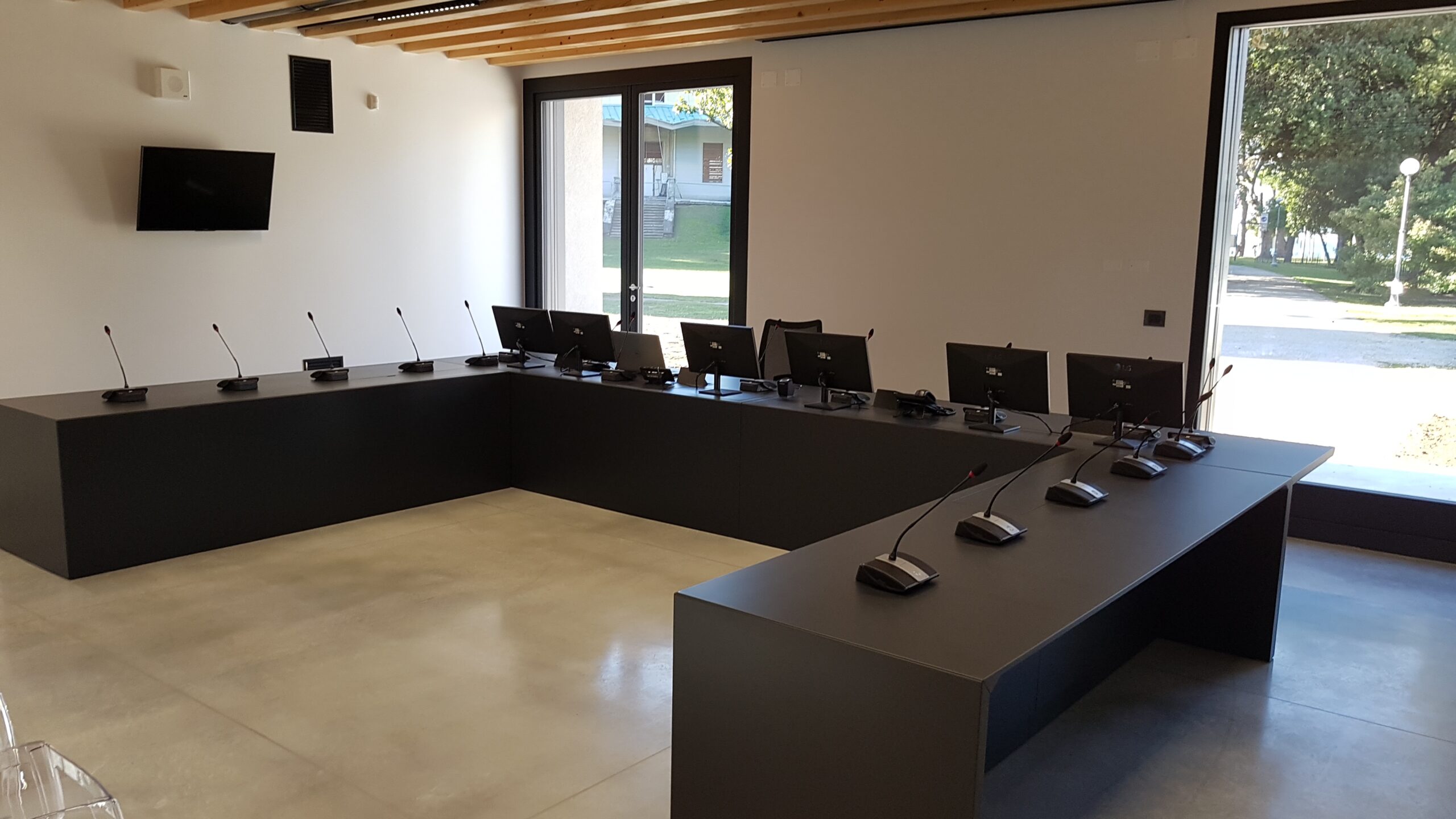 Sala consigliare di Torbole con postazioni conferenza, monitor a parete e ampie vetrate